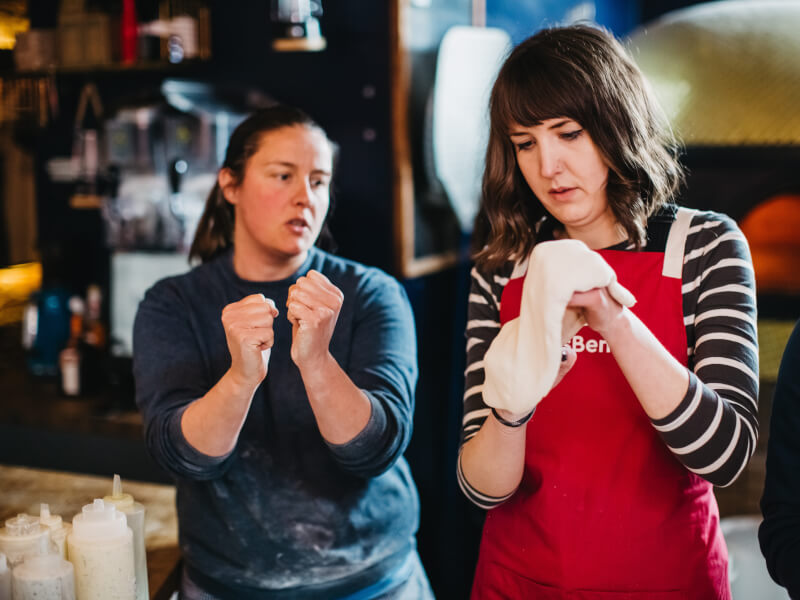 A woman learns how to shape dough in a pizza making class.
